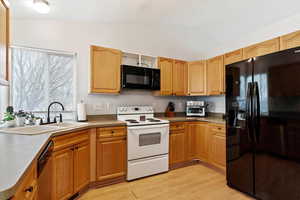 Kitchen featuring black appliances, light hardwood / wood-style floors, sink, and vaulted ceiling