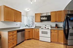 Kitchen with sink, light hardwood / wood-style flooring, lofted ceiling, and black appliances