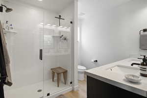 Ensuite bathroom in primary bedroom with glass shower, vinyl floors, dual-sink vanity