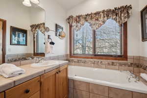 Bathroom featuring vanity, a relaxing tiled tub, and lofted ceiling