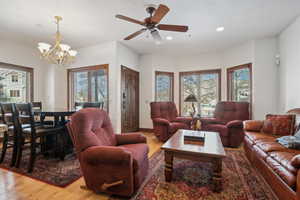 Living room with ceiling fan with notable chandelier, a healthy amount of sunlight, and light wood-type flooring