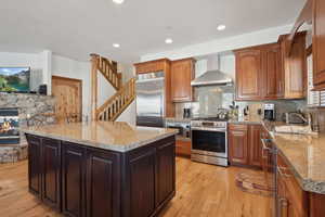 Kitchen with tasteful backsplash, wall chimney exhaust hood, sink, built in appliances, and a center island