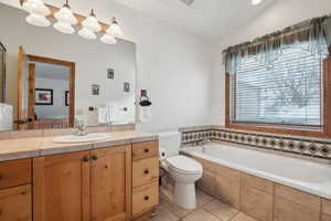 Bathroom featuring vanity, vaulted ceiling, tiled tub, tile patterned flooring, and toilet