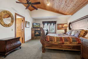 Carpeted bedroom with a fireplace, ceiling fan, lofted ceiling, and wood ceiling