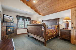 Carpeted bedroom with a fireplace, wooden ceiling, and vaulted ceiling