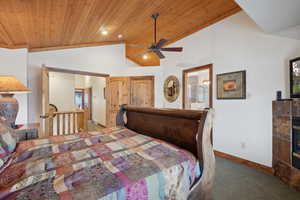 Carpeted bedroom with vaulted ceiling, ensuite bath, ceiling fan, a fireplace, and wood ceiling