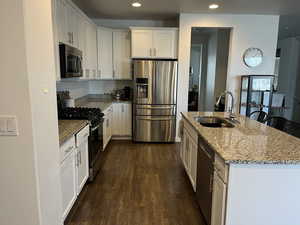 Kitchen featuring appliances with stainless steel finishes, light stone counters, a kitchen island with sink, sink, and white cabinetry