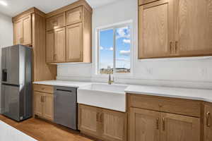 Kitchen with appliances with stainless steel finishes, light hardwood / wood-style flooring, light brown cabinetry, and sink