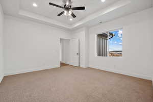 Carpeted spare room with ceiling fan and a tray ceiling