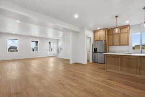 Kitchen featuring stainless steel fridge with ice dispenser, sink, hanging light fixtures, and light wood-type flooring