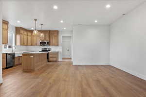 Kitchen with appliances with stainless steel finishes, sink, light hardwood / wood-style floors, a kitchen island, and hanging light fixtures