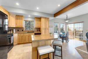 Kitchen featuring black appliances, sink, light brown cabinetry, decorative light fixtures, and a kitchen island