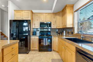 Kitchen with light brown cabinetry, sink, light tile patterned floors, and black appliances