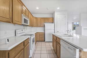 Kitchen featuring sink, white appliances, an island with sink, and light tile patterned floors