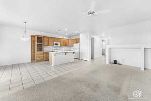 Kitchen featuring a center island, white appliances, ceiling fan, light tile patterned floors, and a kitchen bar