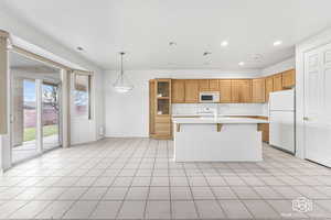 Kitchen with a breakfast bar, white appliances, light tile patterned floors, hanging light fixtures, and an island with sink