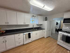 Kitchen featuring tasteful backsplash, white appliances, sink, stacked washer and clothes dryer, and white cabinetry