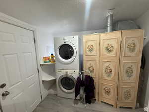 Washroom with cabinets, a textured ceiling, and stacked washing maching and dryer