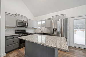 Kitchen with high vaulted ceiling, a center island, light stone countertops, and appliances with stainless steel finishes