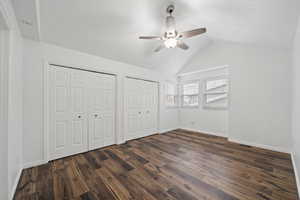 Unfurnished bedroom featuring ceiling fan, dark hardwood / wood-style flooring, lofted ceiling, and two closets