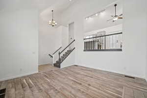 Unfurnished living room with ceiling fan with notable chandelier, high vaulted ceiling, light hardwood / wood-style flooring, and track lighting