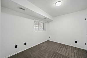 Unfurnished room featuring dark colored carpet and a textured ceiling