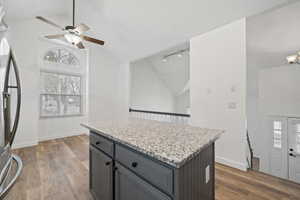 Kitchen featuring stainless steel fridge, vaulted ceiling, ceiling fan, gray cabinets, and a kitchen island