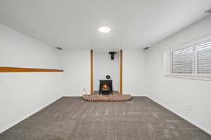 Unfurnished living room featuring carpet floors, a textured ceiling, and a wood stove