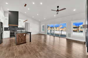 Kitchen featuring white cabinets, vaulted ceiling, ceiling fan, range hood, and a breakfast bar area