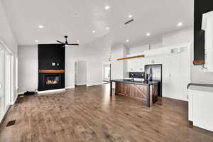 Kitchen with ceiling fan, a large fireplace, a kitchen breakfast bar, a center island with sink, and white cabinets