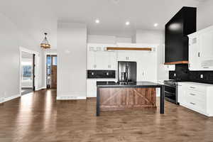 Kitchen featuring a double oven range, a center island with sink, and white cabinets