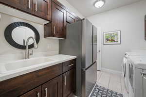 Kitchen with dark brown cabinetry, sink, light tile patterned flooring, and independent washer and dryer