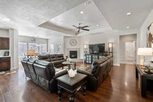 Living room with a tile fireplace, dark hardwood / wood-style flooring, a tray ceiling, and ceiling fan