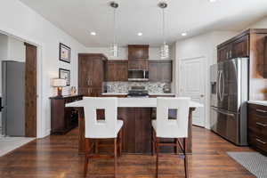 Kitchen with appliances with stainless steel finishes, dark brown cabinetry, tasteful backsplash, and a kitchen island