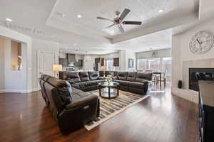 Living room with ceiling fan, dark wood-type flooring, a textured ceiling, a tray ceiling, and a tiled fireplace