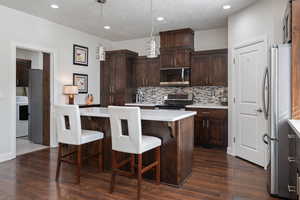 Kitchen featuring stainless steel appliances, washer / clothes dryer, decorative light fixtures, dark brown cabinets, and a kitchen island