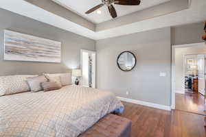 Bedroom featuring a walk in closet, dark hardwood / wood-style flooring, a tray ceiling, and ceiling fan