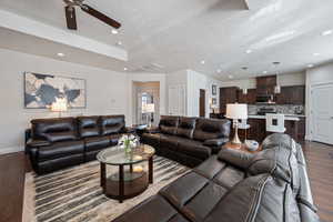 Living room featuring a textured ceiling, a tray ceiling, ceiling fan, and dark wood-type flooring