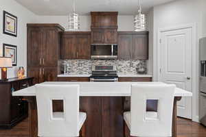 Kitchen featuring a center island, stainless steel appliances, pendant lighting, decorative backsplash, and dark brown cabinets