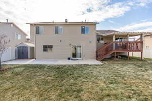 Back of property featuring a lawn, a shed, a patio, and a wooden deck