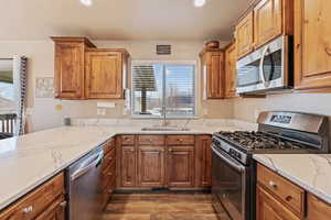 Kitchen featuring appliances with stainless steel finishes, light stone counters, dark wood-type flooring, and sink