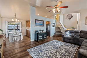 Living room featuring ceiling fan with notable chandelier, dark wood-type flooring, and lofted ceiling