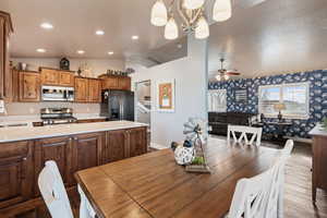 Dining space with light wood-type flooring, ceiling fan with notable chandelier, lofted ceiling, and sink