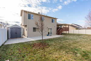 Rear view of property with a lawn, a storage unit, a deck, and a patio