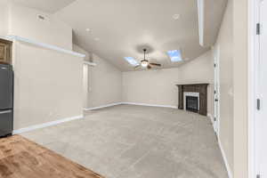 Unfurnished living room with light colored carpet, ceiling fan, and vaulted ceiling with skylight