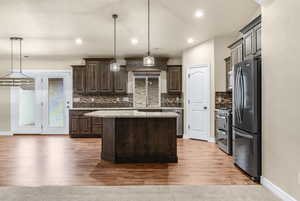 Kitchen with hanging light fixtures, a center island, stainless steel appliances, and dark brown cabinets