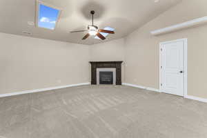 Unfurnished living room featuring a tiled fireplace, ceiling fan, light colored carpet, and lofted ceiling