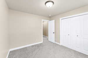 Unfurnished bedroom featuring a textured ceiling, light carpet, and a closet