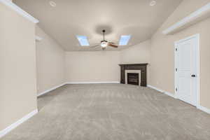 Unfurnished living room featuring vaulted ceiling with skylight, ceiling fan, light carpet, and a tiled fireplace