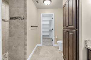 Bathroom featuring vanity, tile patterned flooring, toilet, a textured ceiling, and a tile shower